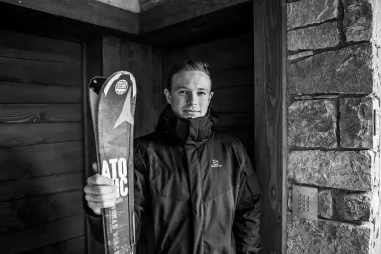 Ski concierge holding skis outside stone and timber chalet, ready to assist guests with equipment and mountain activities