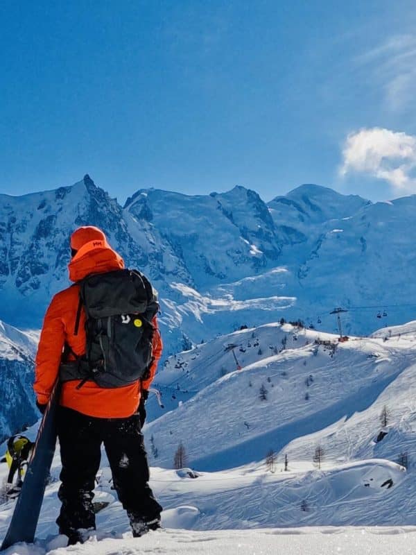 Skier in bright orange jacket admiring snow-covered Alpine peaks and ski slopes in Chamonix