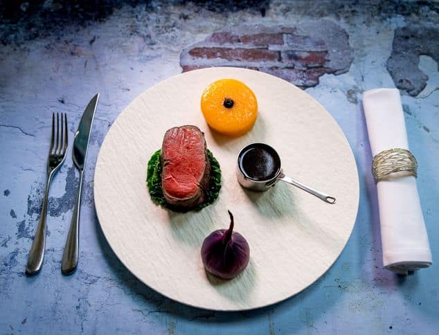 Fine dining beef fillet with wilted greens, roasted tomato and jus served on a round wooden board at a Dorset holiday let