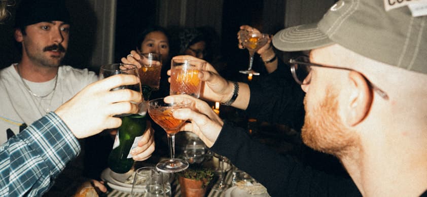 Group of friends raising cocktail glasses in a celebratory toast at an evening dinner party, perfect for milestone holiday g…