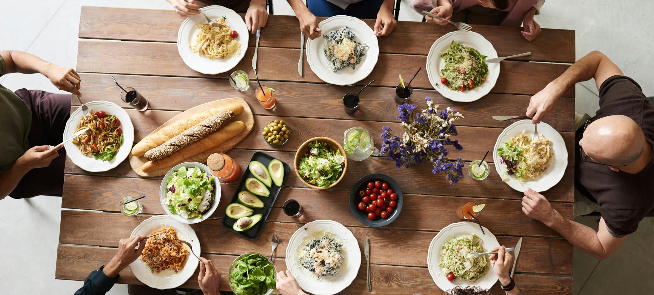 Overhead view of family dining together at rustic wooden table with pasta dishes, fresh salads and wine