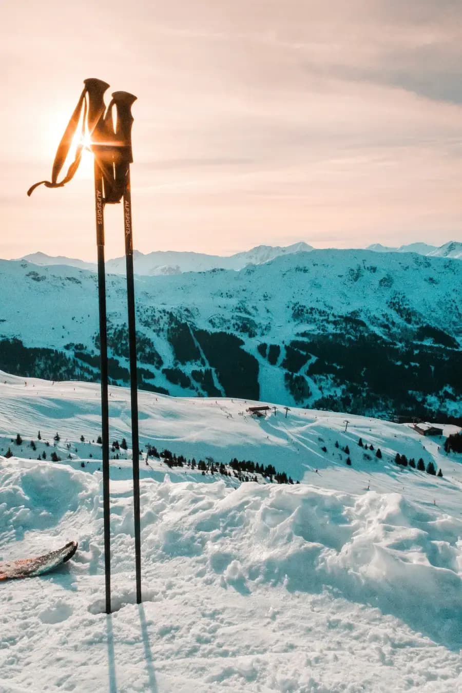 Ski poles planted in fresh powder snow at sunset overlooking Alpine peaks and ski slopes in the French Alps
