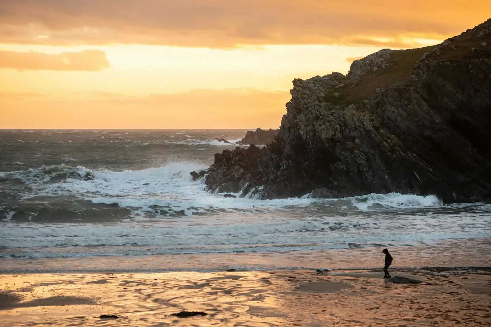 Dramatic Welsh coastline at sunset with rugged cliffs, crashing waves and golden sky creating perfect coastal holiday backdr…