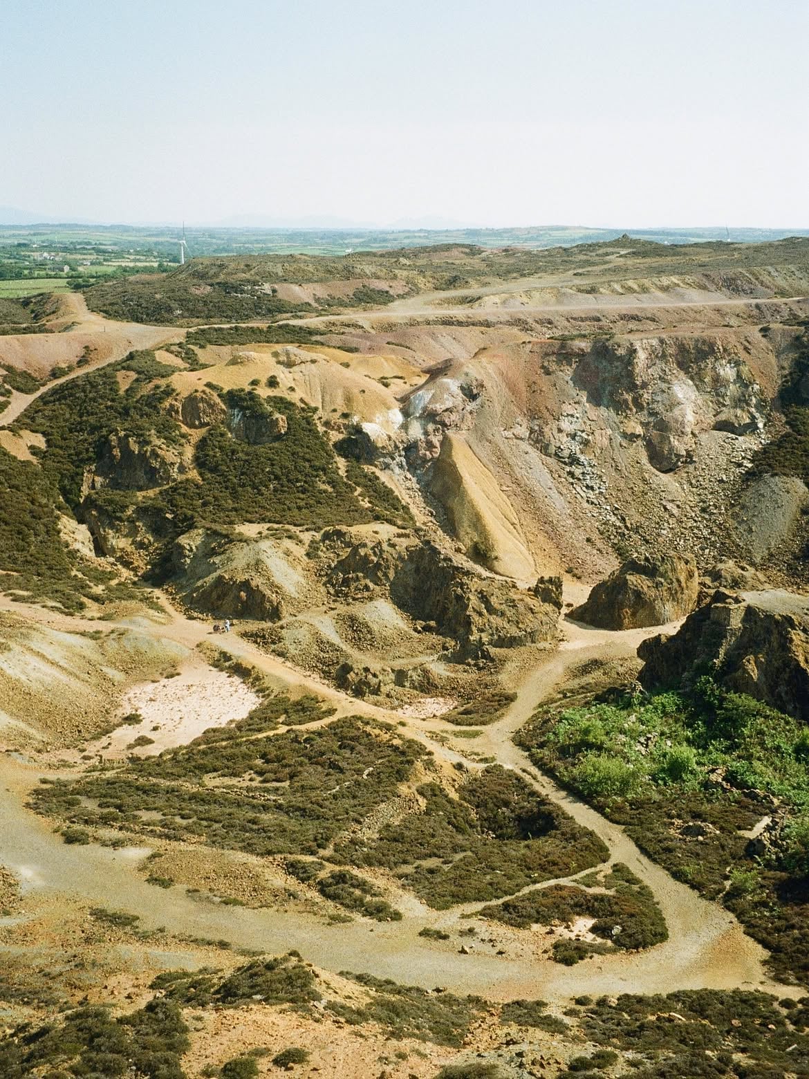 Dramatic open-cast copper mine landscape at Parys Mountain, Anglesey, with vivid ochre and rust-coloured rock formations str…