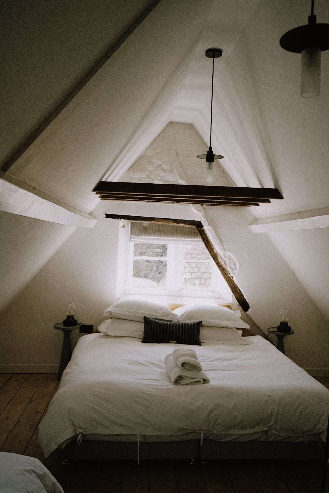 Attic bedroom in a character cottage with vaulted whitewashed ceiling, exposed timber beams, and crisp white bedding beneath…