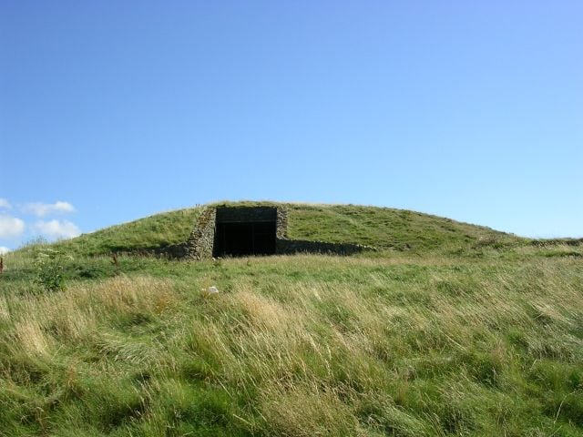 Ancient Neolithic burial mound at Barclodiad y Gawres, Anglesey, with a stone-framed entrance set into a grass-covered hillo…