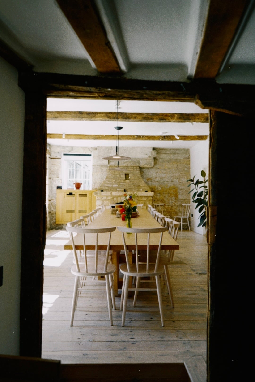 Large communal dining room in a converted stone barn with exposed beams, long wooden table seating up to 20 guests, and a st…