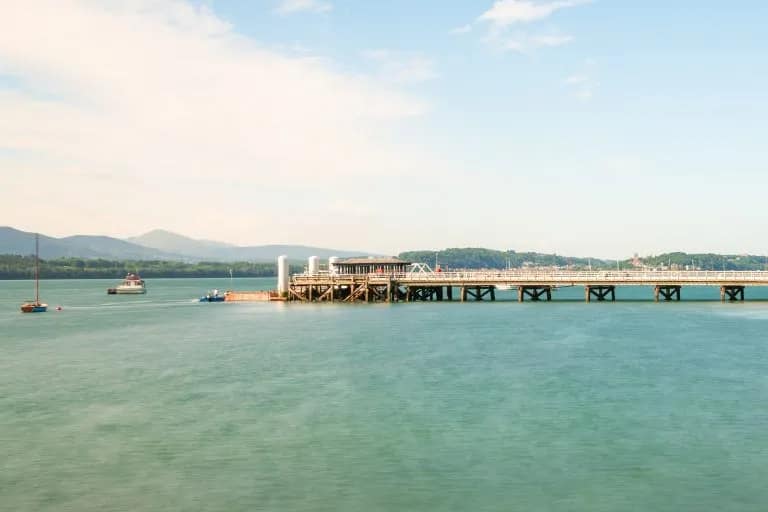 Beaumaris pier stretching into calm turquoise waters with sailing boats and mountain backdrop on Anglesey