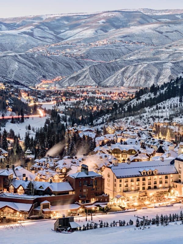 Snow-covered luxury ski resort village nestled in mountain valley with illuminated chalets and hotels at dusk
