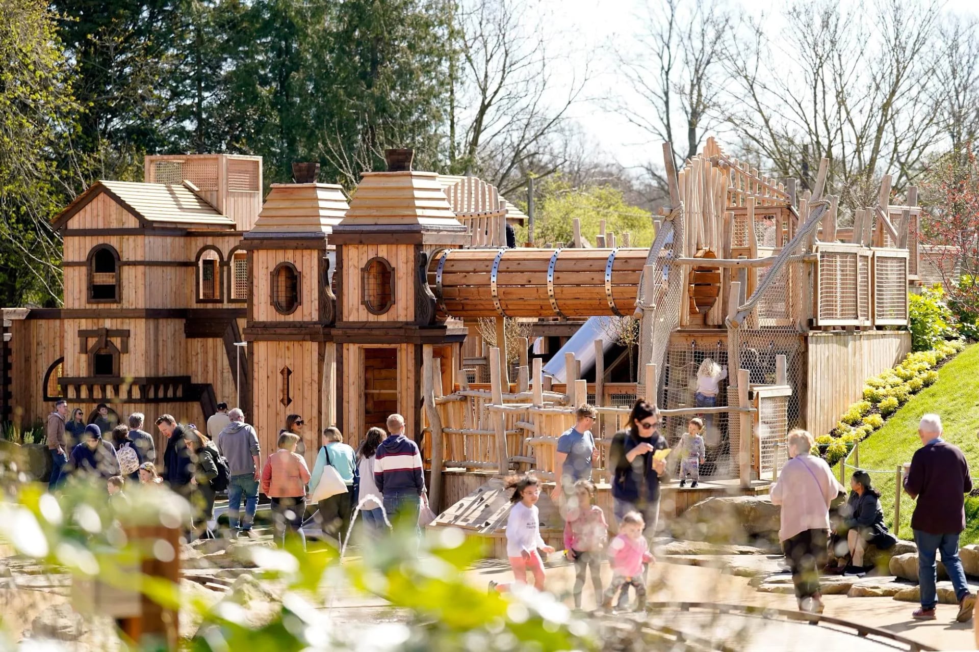 Families exploring the large wooden adventure playground at Blenheim Palace, Oxfordshire, on a sunny spring day