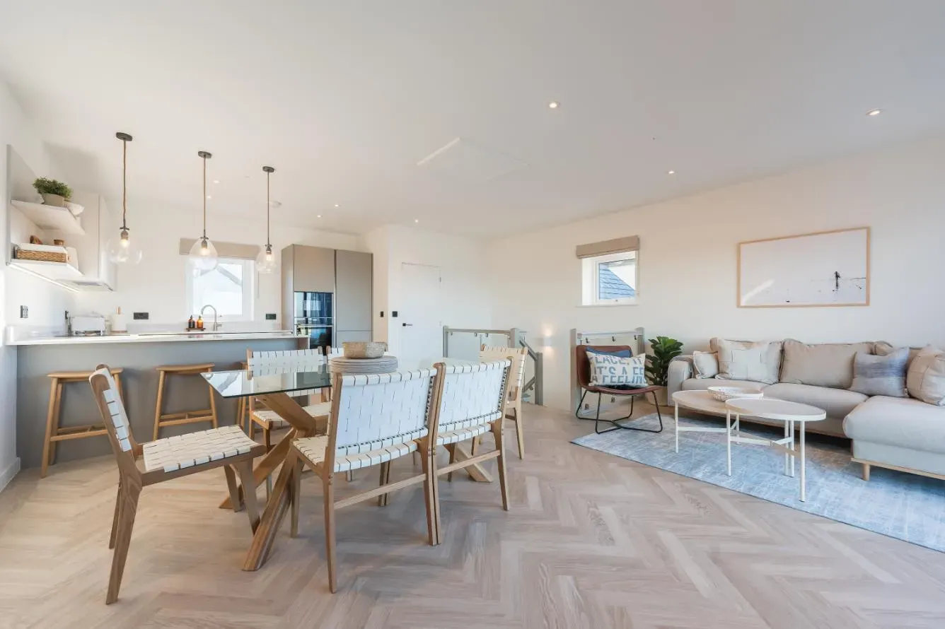 Open-plan living and dining area in a luxury holiday let with herringbone oak flooring, woven leather chairs, glass dining t…