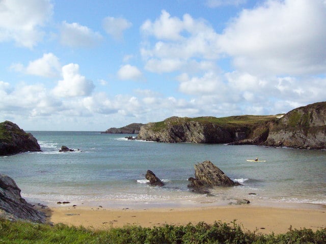 Secluded sandy cove at Cable Bay, Anglesey, with dramatic rocky headlands and a kayaker on calm turquoise water