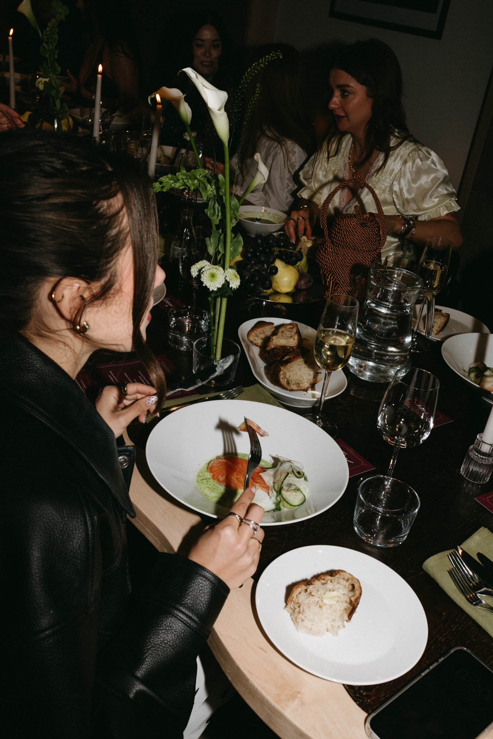 Guests enjoying a candlelit dinner party with salmon starter, white wine, and calla lily floral centrepiece