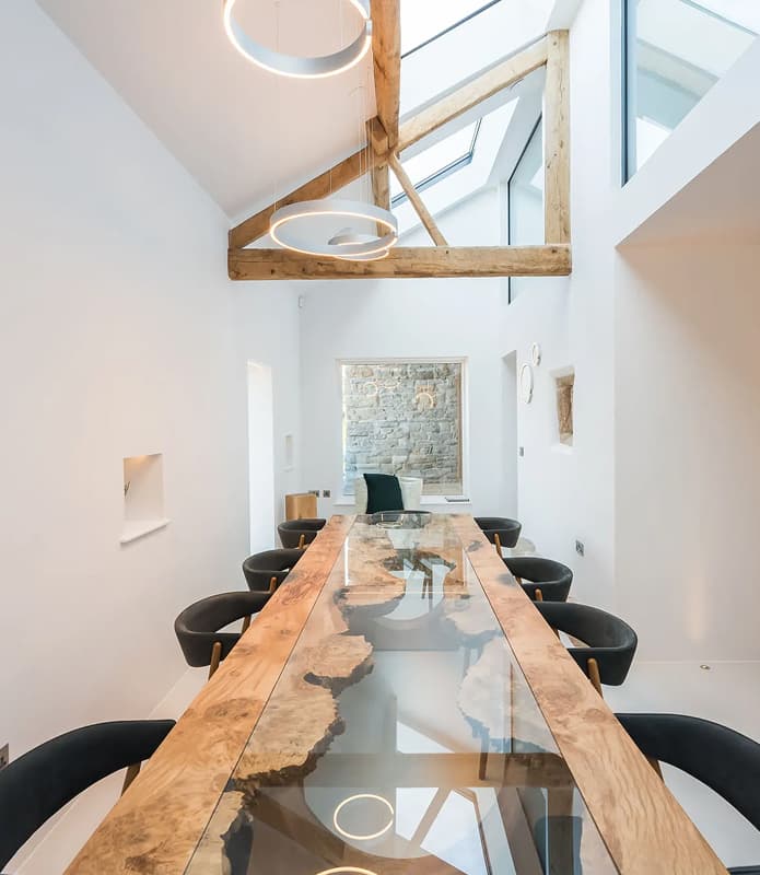 Dining room in a converted barn holiday let with a live-edge resin dining table, exposed timber beams, skylights, and circul…