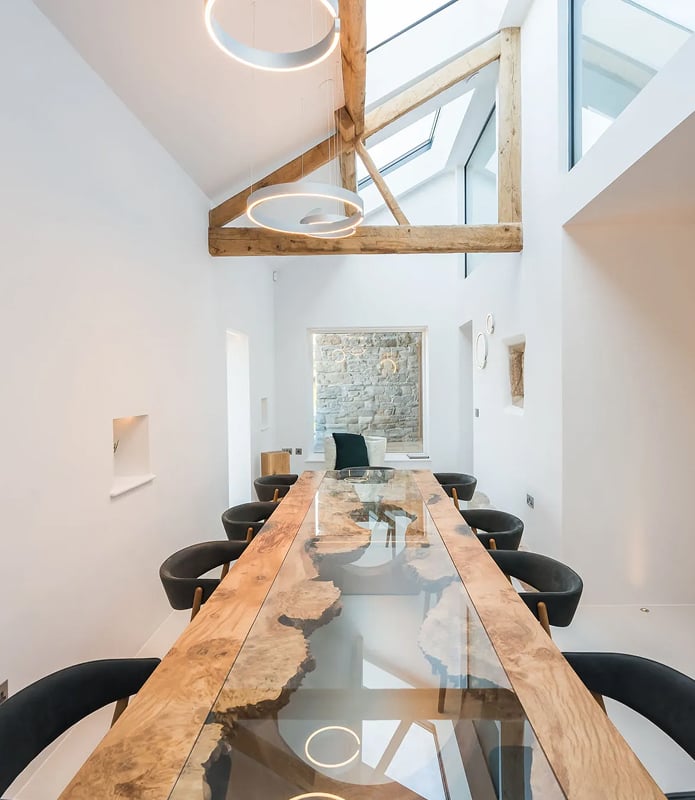 Dining room in a converted barn holiday let with a live-edge resin dining table, exposed timber beams, skylights, and circul…