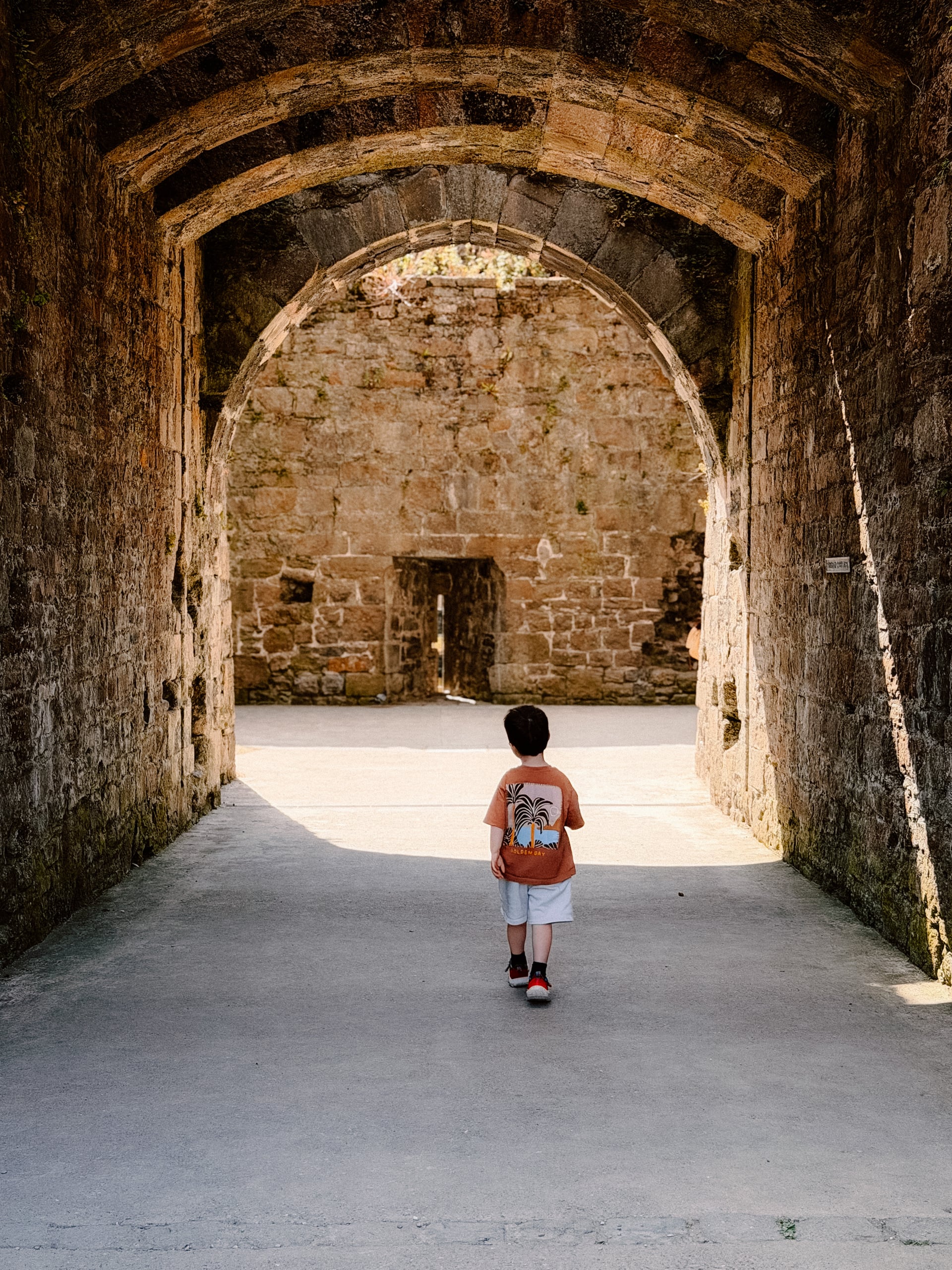 Young child walking through a medieval stone archway into sunlit castle ruins, perfect for family-friendly holiday explorati…