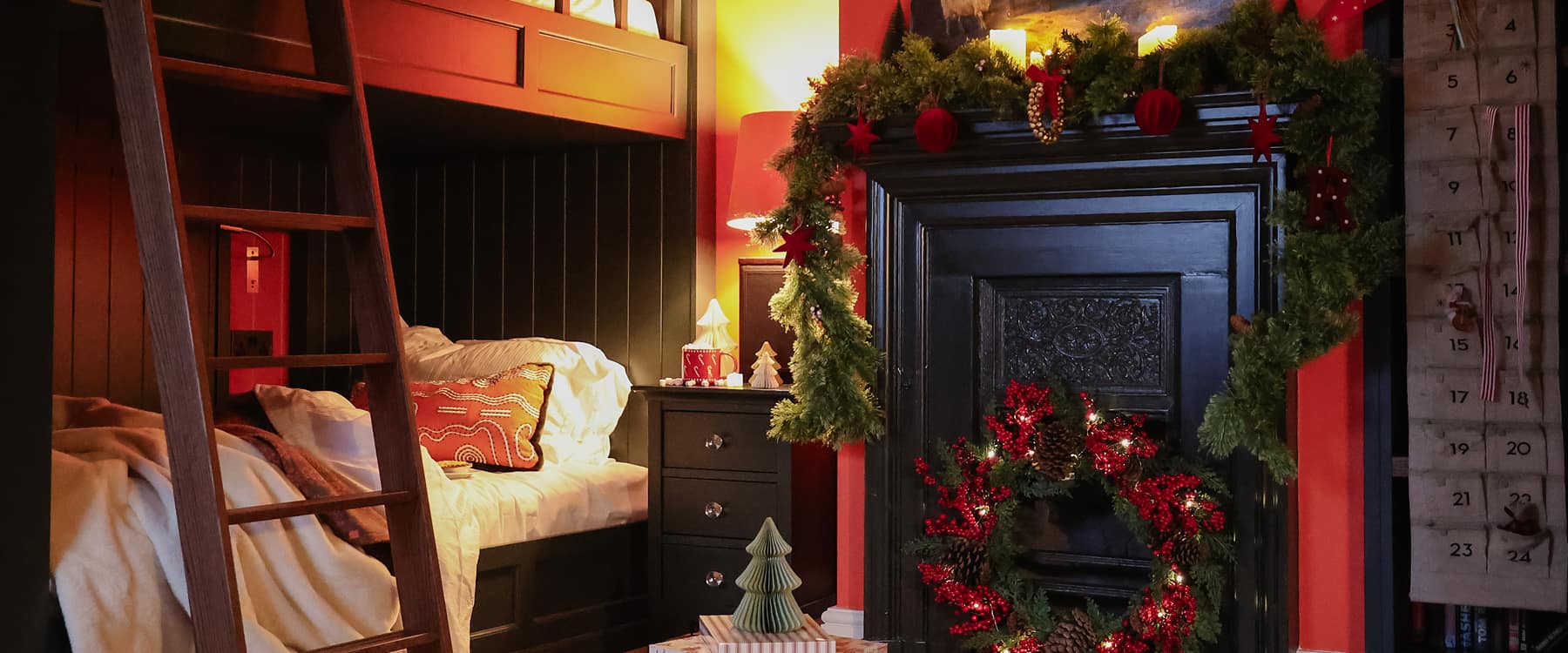 Festively decorated children's bunk bed room with Christmas garlands, lit wreath, advent calendar, and warm candlelight in a…