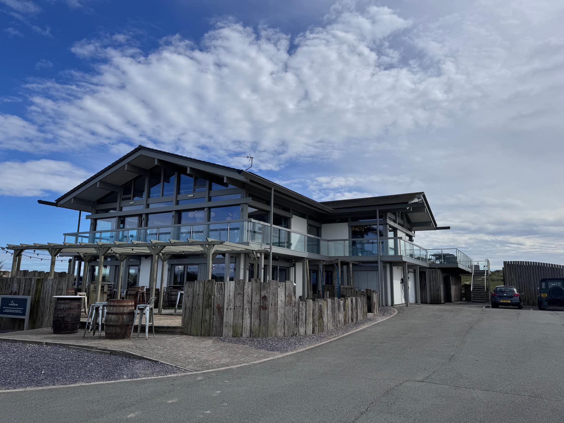 Contemporary coastal restaurant and bar with floor-to-ceiling glazing, wraparound glass balcony, and outdoor terrace with pe…