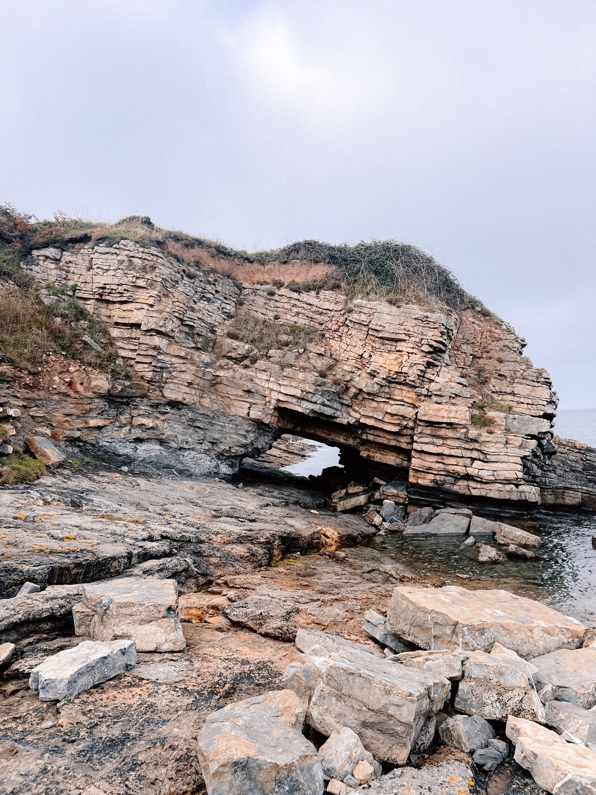 Layered sandstone rock arch on a rugged UK coastline, with tidal pools and scattered boulders ideal for coastal walks