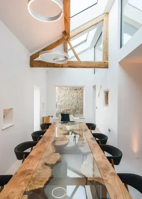 Converted barn dining room with live-edge resin table, exposed oak beams, skylights, and original stone wall feature
