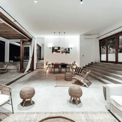 Modern open-plan living space with polished concrete floors, exposed timber beams, and woven furniture overlooking outdoor t…