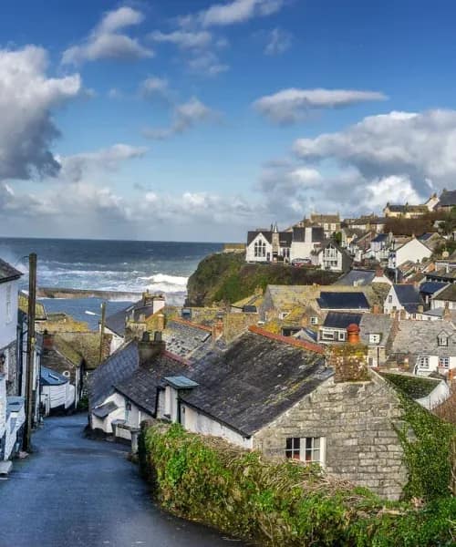 Stone cottages cascade down hillside to harbour in Port Isaac, Cornwall, with dramatic coastline and ocean waves