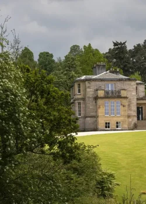 Grand Georgian country house with tall sash windows and sandstone facade set within sweeping lawns and mature woodland