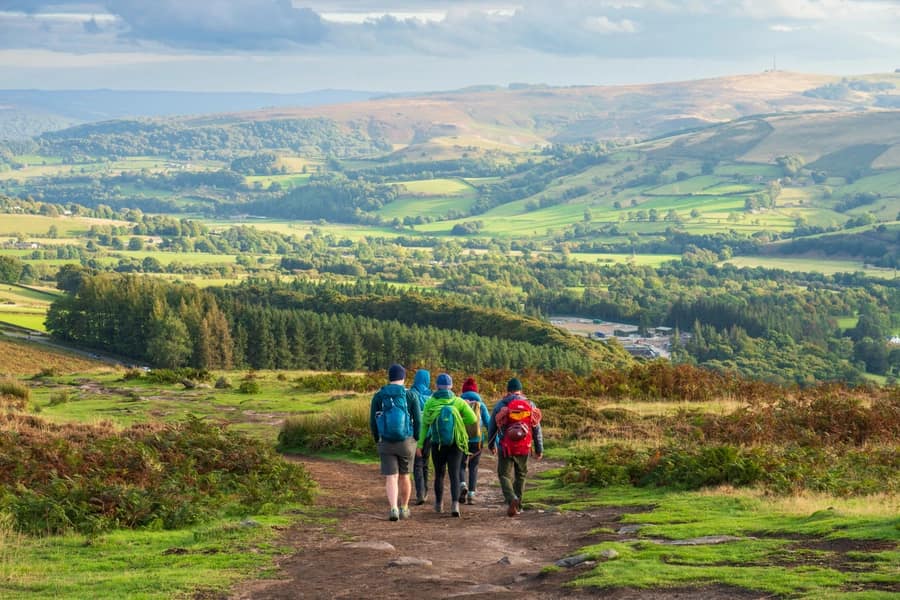 Group of walkers with rucksacks descending a moorland path into the sweeping green valleys of the Peak District