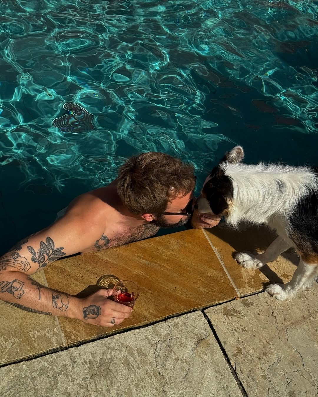 Guest relaxing in a private outdoor pool with a cocktail, sharing a moment with a dog on the stone poolside terrace