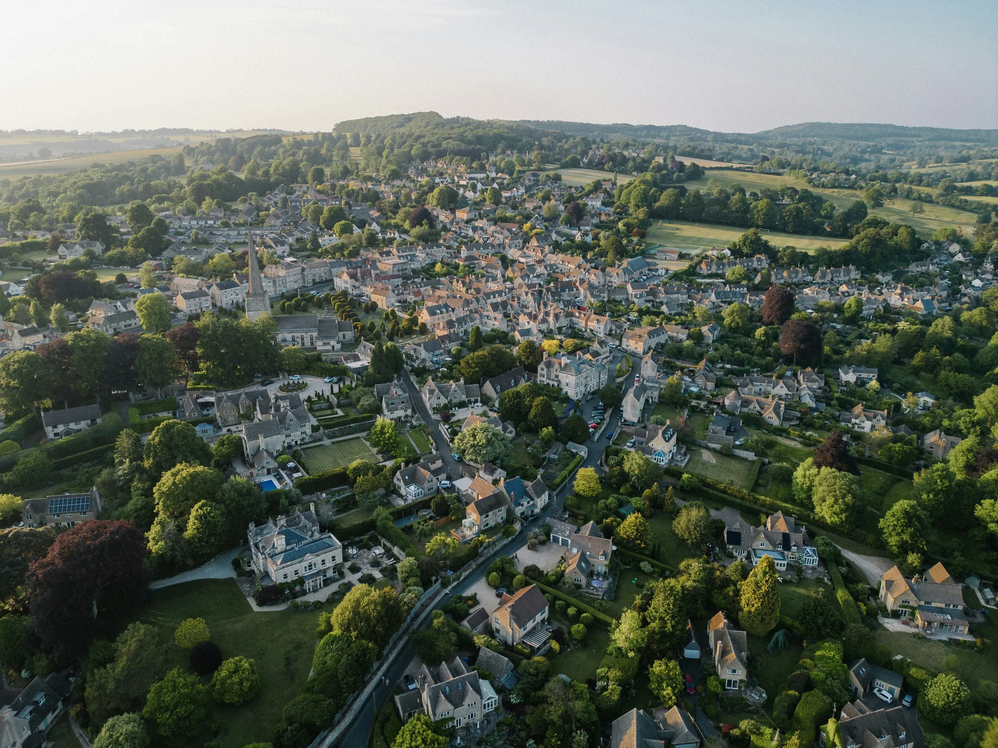 Aerial view of picturesque English market town nestled in rolling green countryside with historic church spire and tradition…