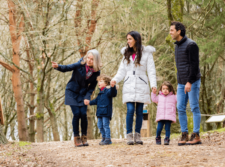 Three-generation family enjoying a winter woodland walk, grandmother pointing out wildlife to young children among bare trees