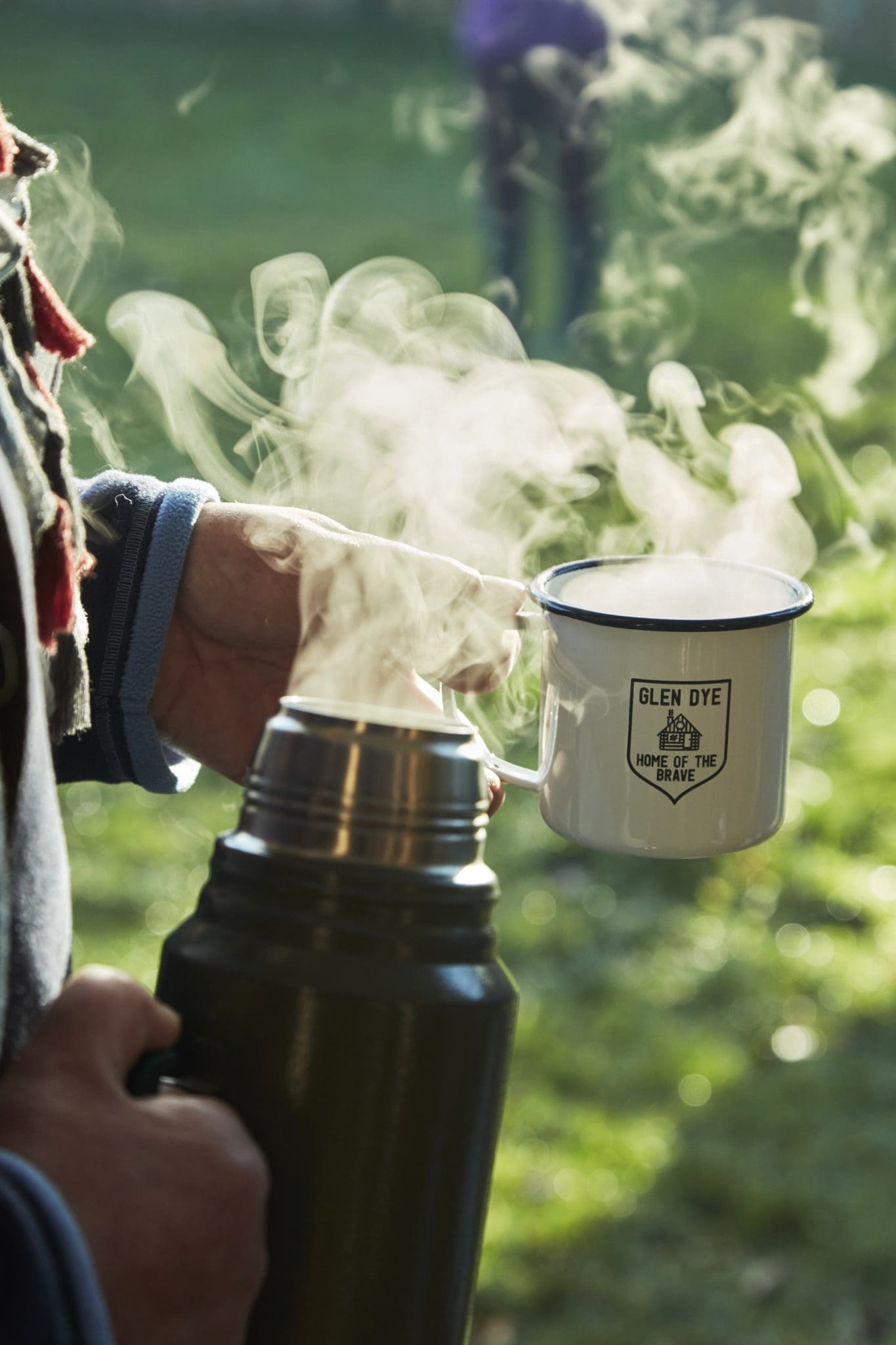 Guest holding a steaming Glen Dye enamel mug outdoors beside a flask, perfect for crisp Scottish countryside mornings