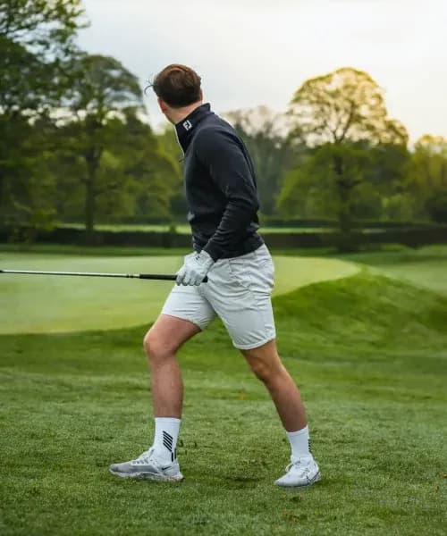 Golfer mid-swing on pristine countryside course with rolling greens and mature trees