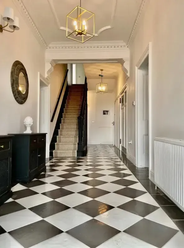 Grand entrance hallway with polished black and white chequered floor tiles, ornate cornicing, and brass geometric pendant li…