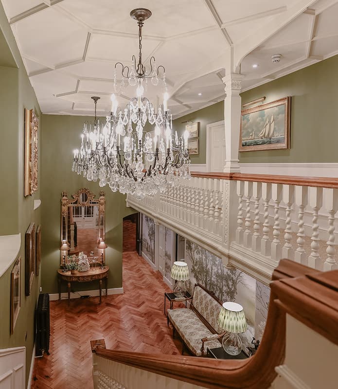 Grand hallway with crystal chandelier, coffered ceiling, herringbone parquet floor, and white balustrade staircase in a luxu…