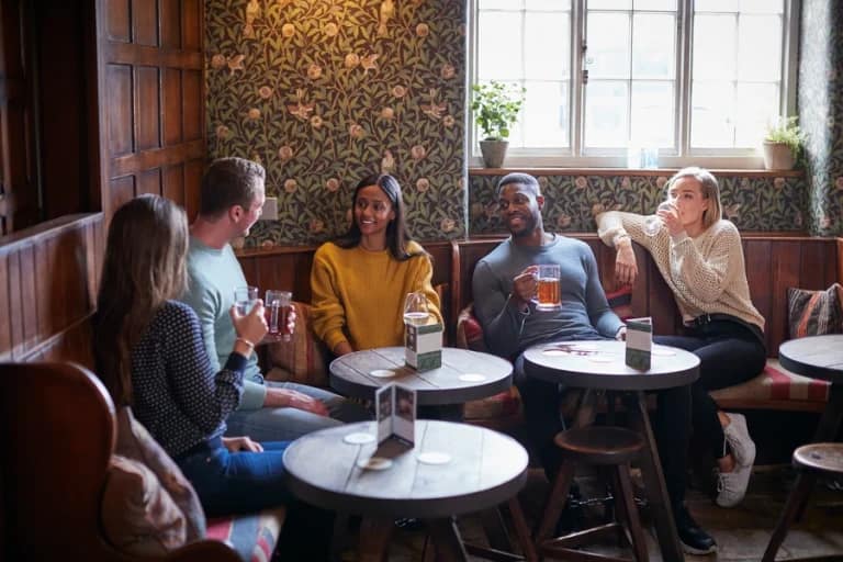 Group of friends enjoying drinks together in a cosy traditional British pub with wood panelling and floral wallpaper