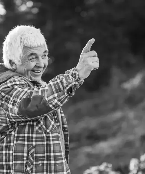 Smiling older man in a checked shirt giving a thumbs up outdoors, conveying guest satisfaction