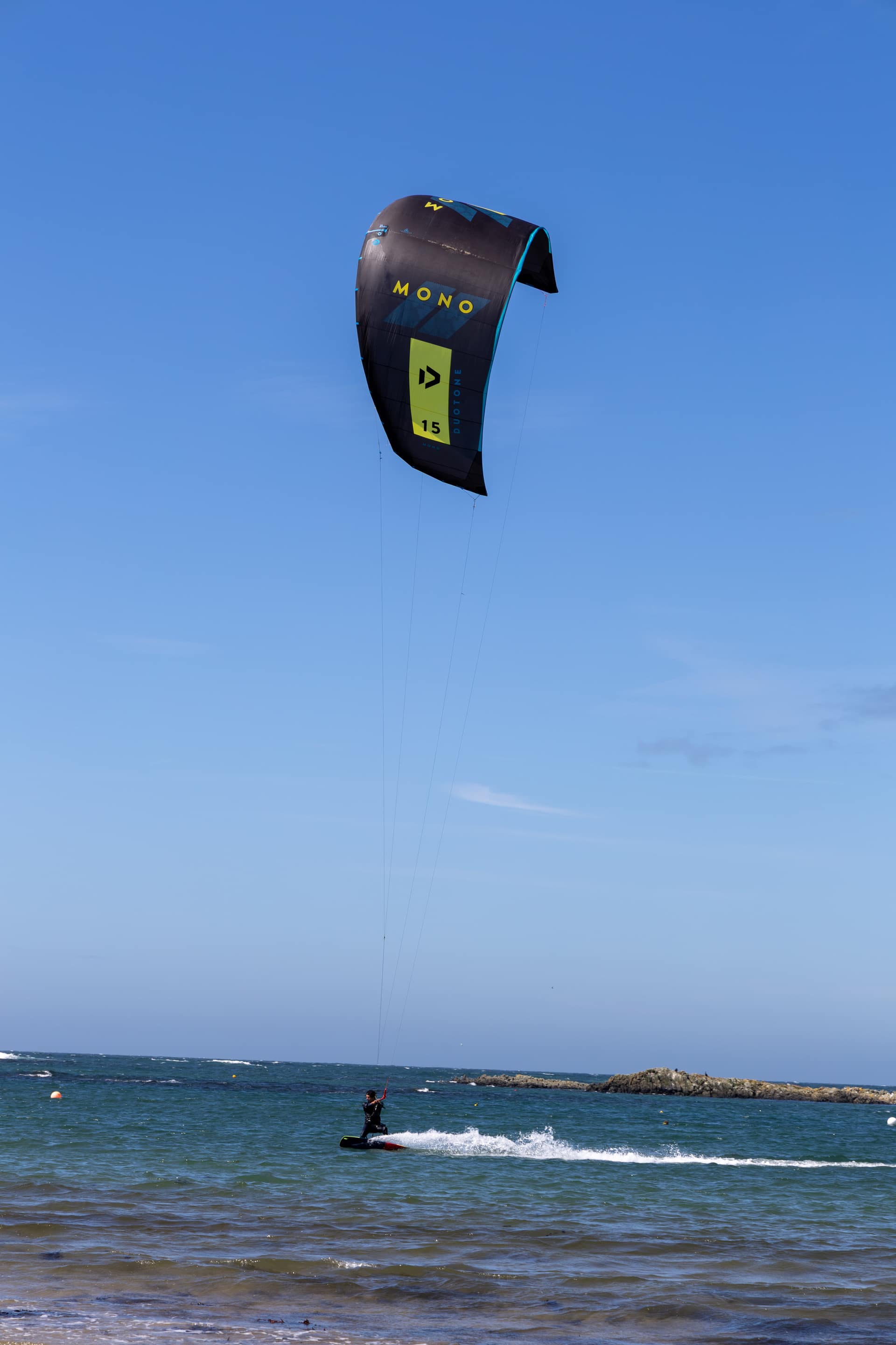 Kitesurfer riding coastal waters beneath a large Duotone Mono kite on a sunny day, ideal for active seaside holidays