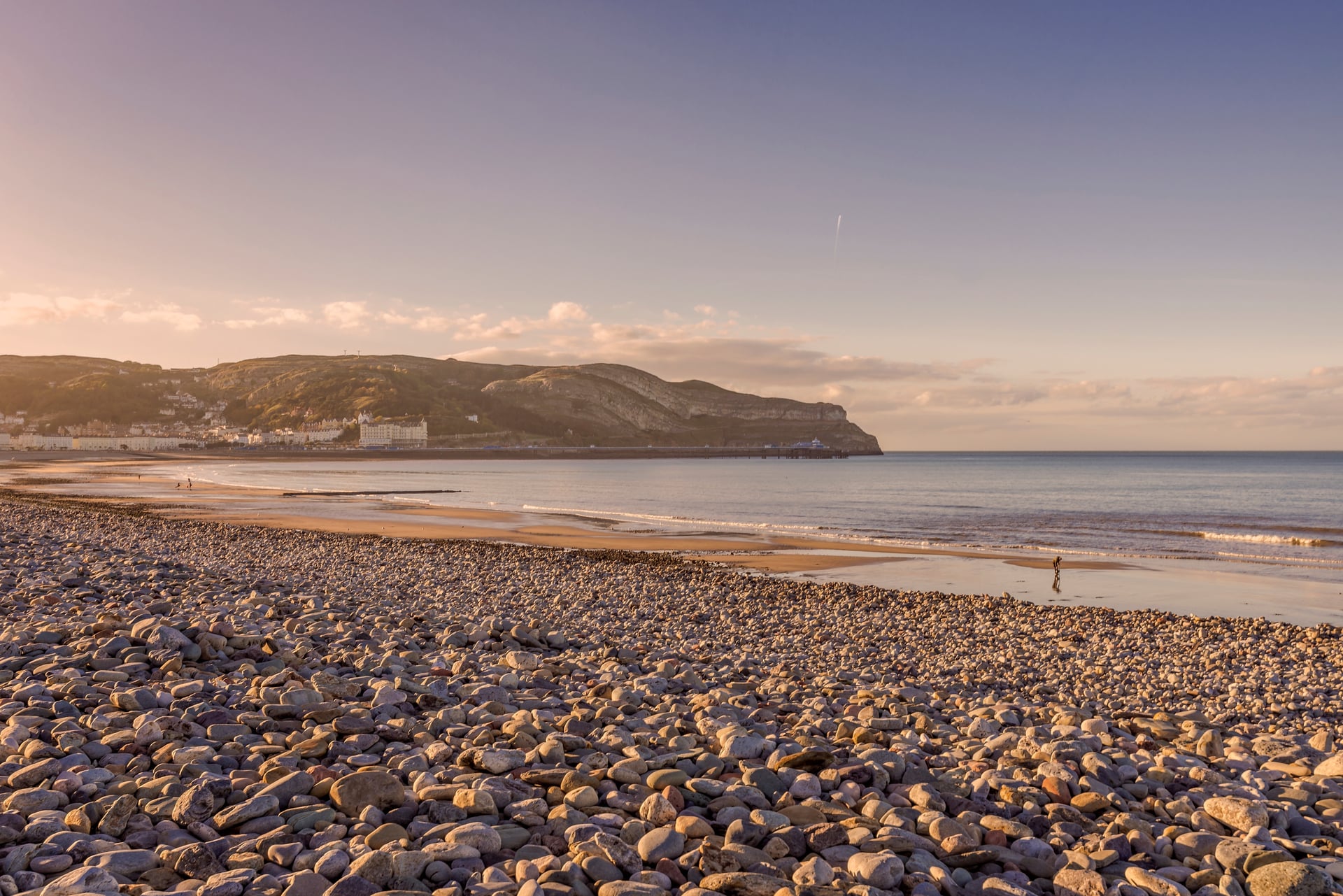 Llandudno beach at golden hour with pebble shoreline, sweeping bay, Victorian pier and the Great Orme headland beyond