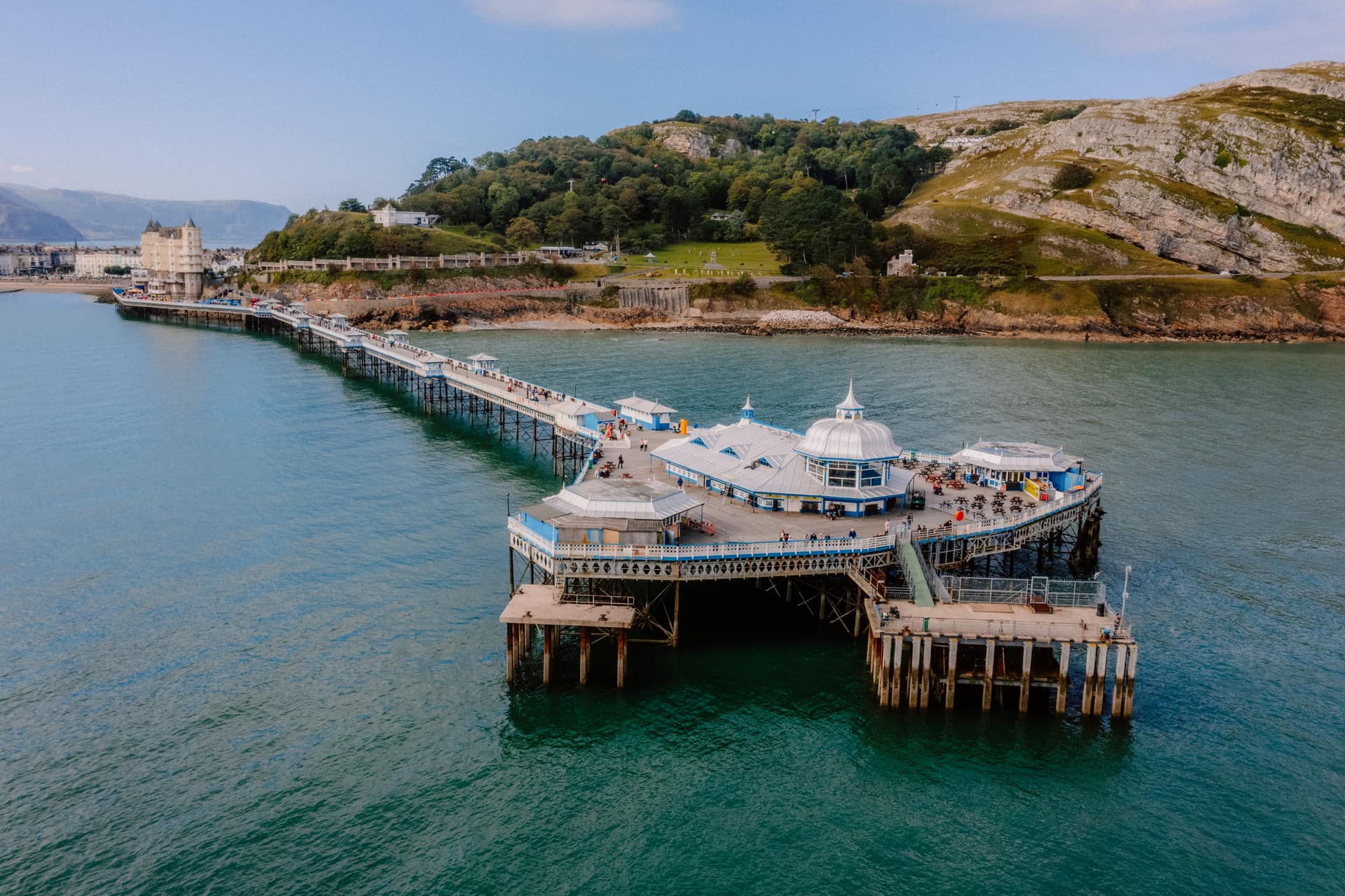 Aerial view of Llandudno Pier stretching into turquoise waters with the Great Orme headland behind, North Wales