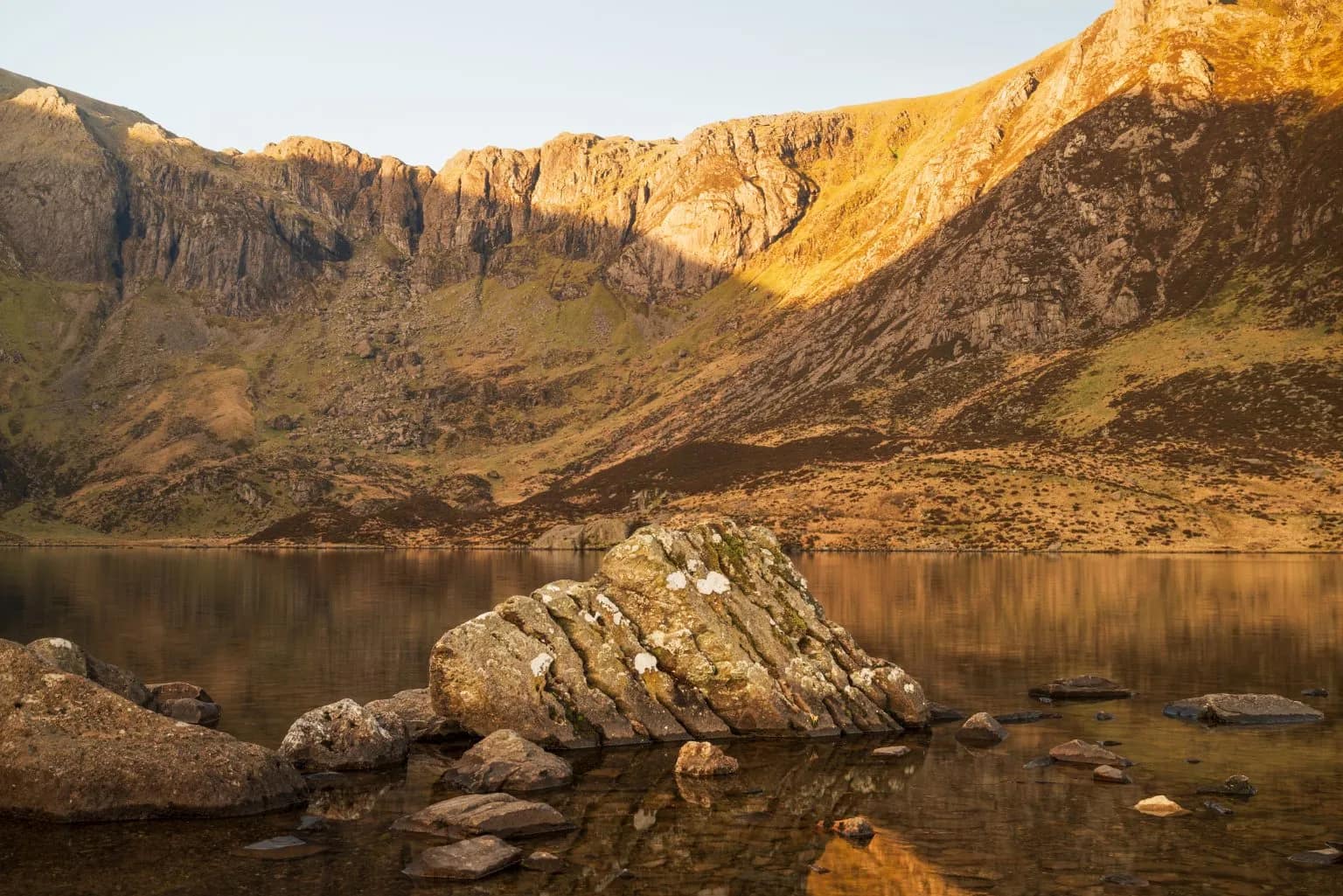 Golden hour light on the rocky crags above Llyn Idwal, Snowdonia, with lichen-covered boulders at the still lake's edge