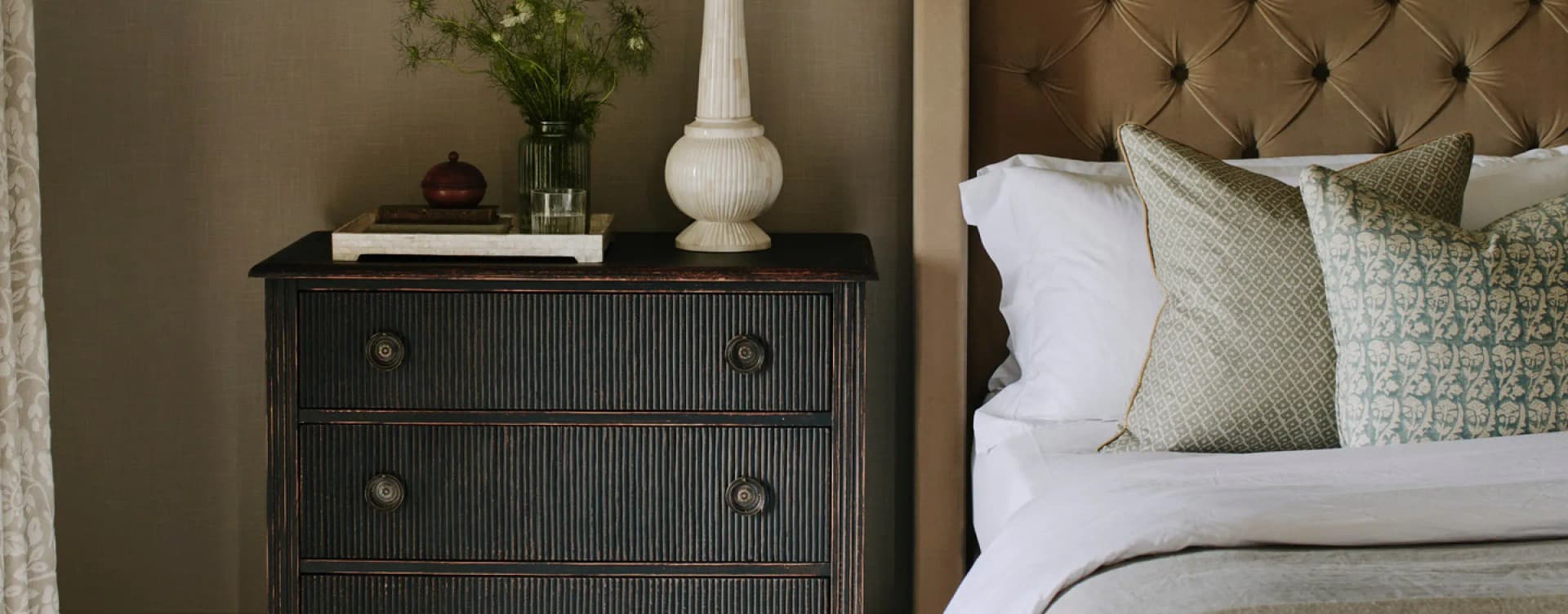 Luxury holiday let bedroom detail with tufted velvet headboard, crisp white linen, patterned cushions, and an ebonised bedsi…