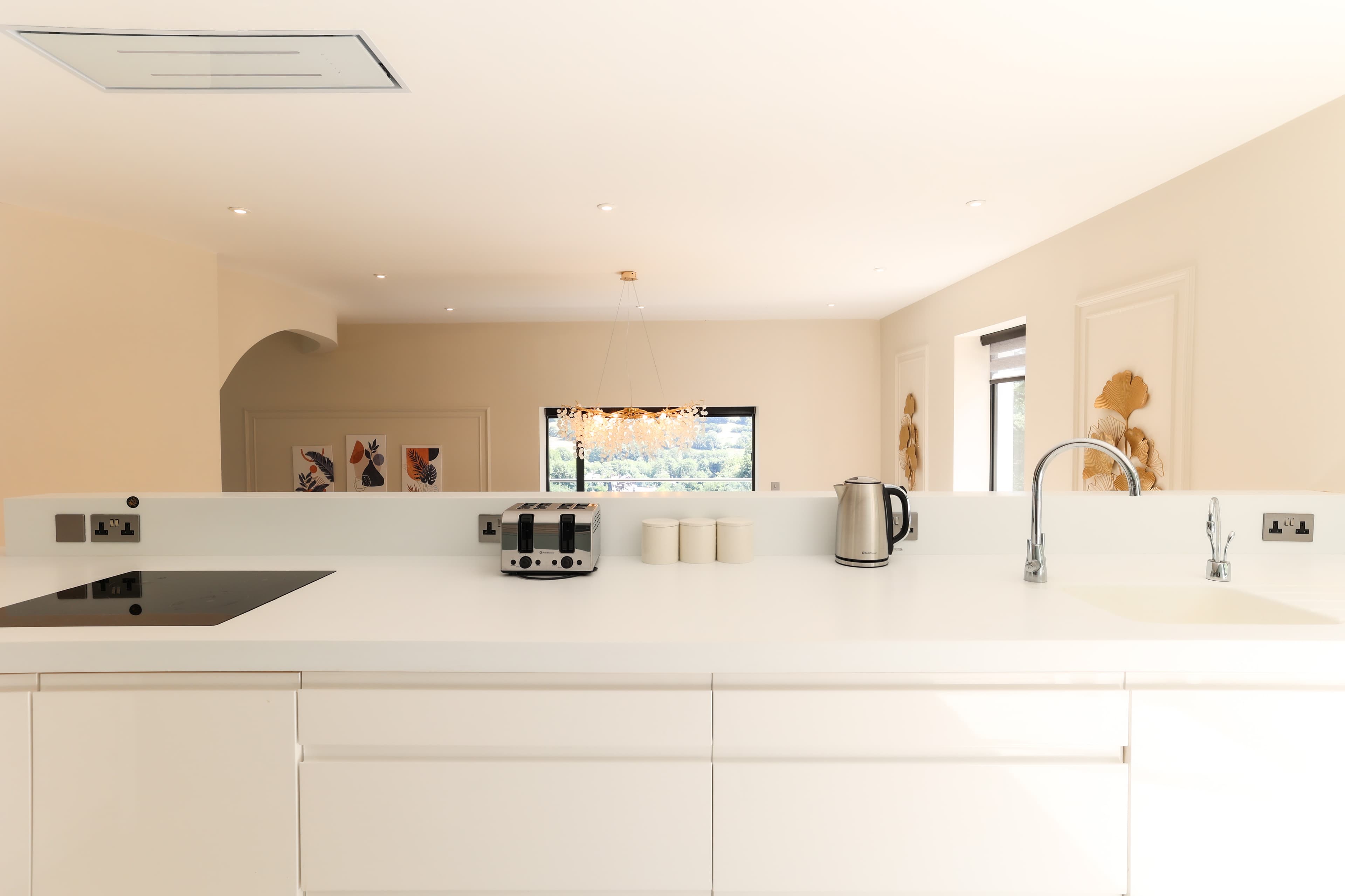 Sleek white kitchen island with induction hob, four-slice toaster, kettle, and chrome tap, with countryside views through th…