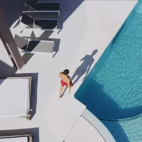 Aerial view of luxury villa pool terrace with guest relaxing by turquoise swimming pool and modern sunloungers