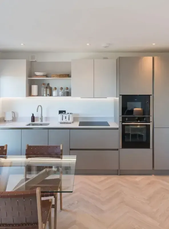 Sleek handleless kitchen with integrated double oven, induction hob, and herringbone parquet flooring in a luxury holiday let