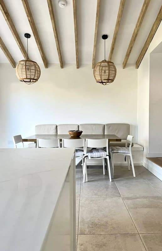 Bright open-plan dining area with exposed wooden ceiling beams, rattan pendant lights, built-in upholstered bench seating an…