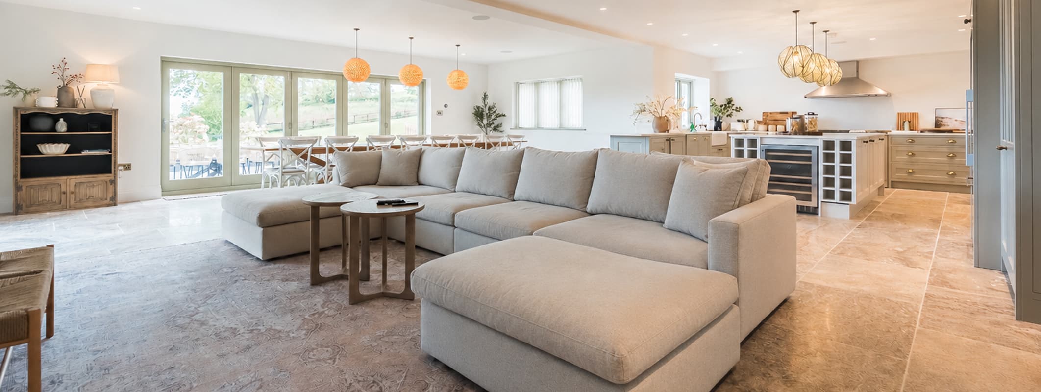 Spacious open-plan living, dining and kitchen area in a luxury UK holiday cottage, featuring a large corner sofa, woven pend…