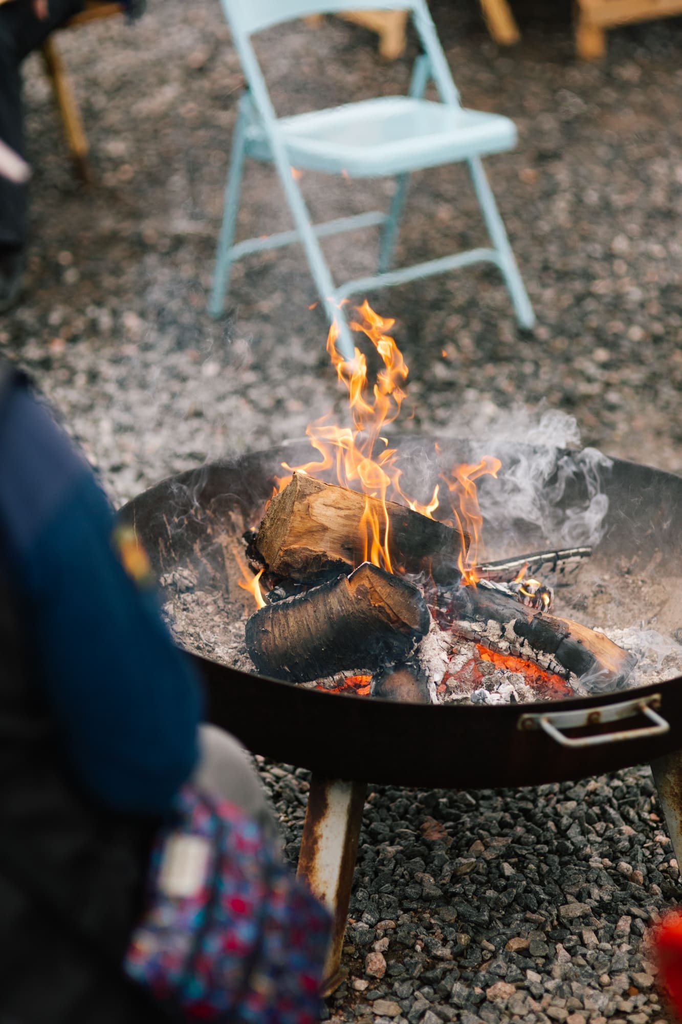 Outdoor fire pit with crackling log flames on a gravel terrace, perfect for cosy evening gatherings at a holiday let