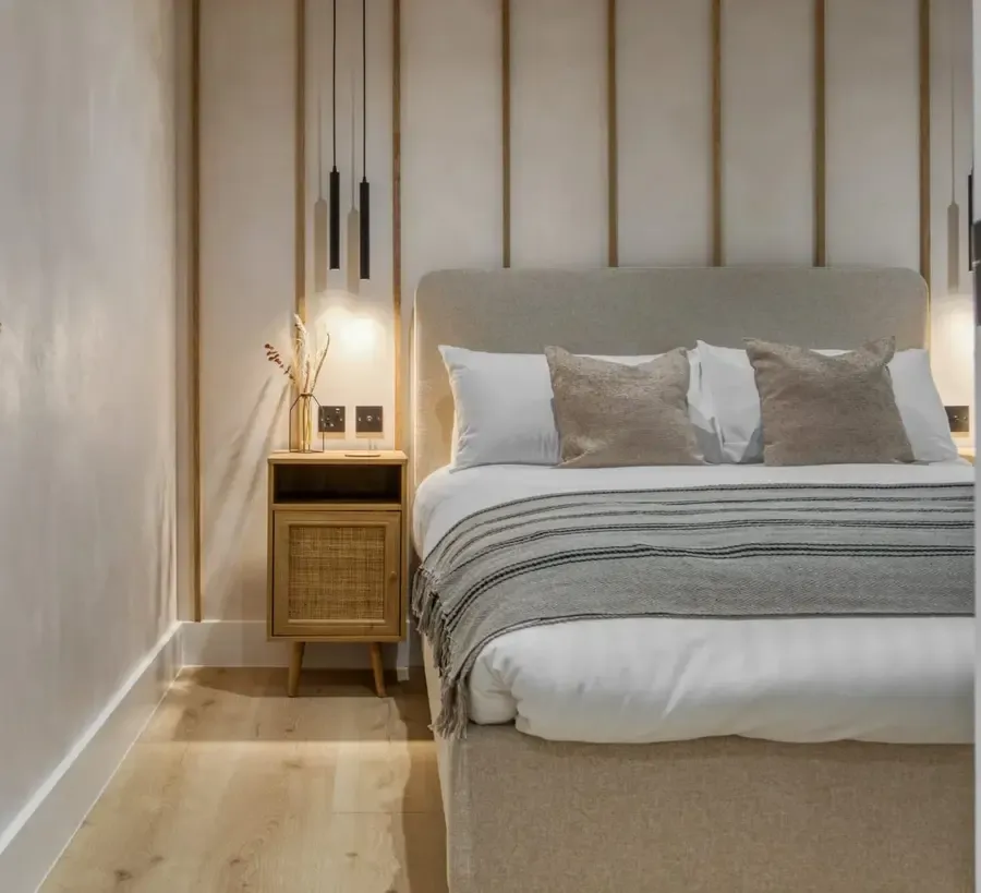 Luxury double bedroom with upholstered headboard, rattan bedside cabinet, pendant lighting, and neutral tones in a holiday l…