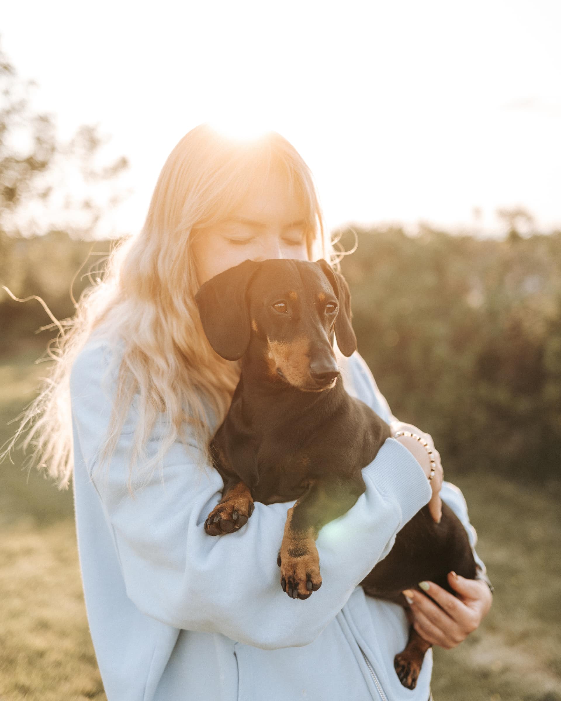 Woman cradling a dachshund outdoors at golden hour, evoking the pet-friendly welcome of a Birch Stays holiday let